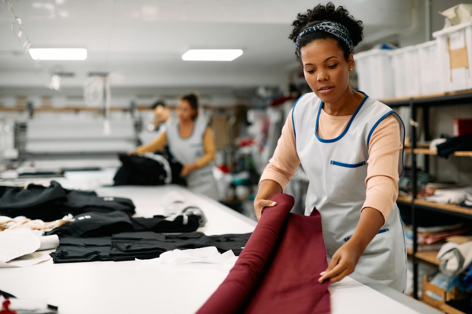 Young African American seamstress working with fabric at clothing design workshop.